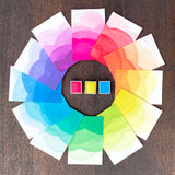Ombre swatches of watercolour paint making up a colour wheel of Neon colourway, surrounding Hot Pink, Lemon Yellow and Lagoon watercolour half pans, on a dark wooden background.