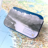 A closed Sketching tin with an illustration depicting the mountainous shoreline of the Sunshine Coast BC, on a vintage map of the Pacific Northwest.