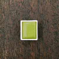 Chartreuse Green watercolour half pan on a rustic wooden background.