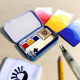 The sketching tin in use, with red yellow and blue watercolour paints and swatches.