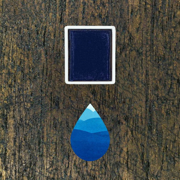 Cerulean watercolour half pan above a droplet shaped ombre swatch in Cerulean watercolour paint, on a rustic dark wooden background.