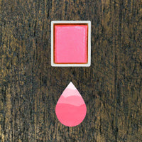 Bubblegum watercolour half pan above a droplet shaped ombre swatch in Bubblegum watercolour paint, on a rustic dark wooden background.